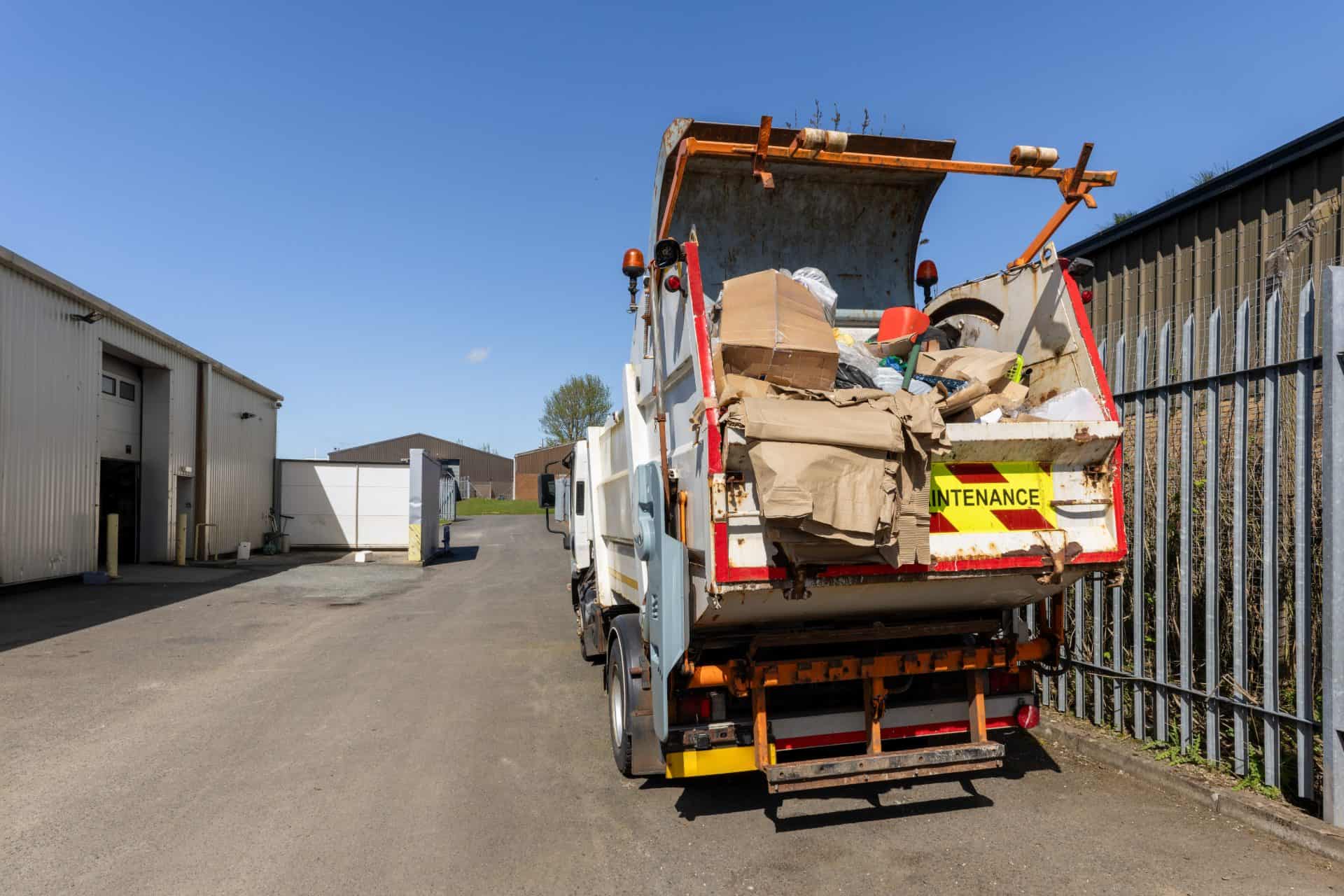 Rear view of refuse or recycling truck carrying cardboard and waste materials in an industrial storage yard, illustrating recycling, waste management and commercial operations